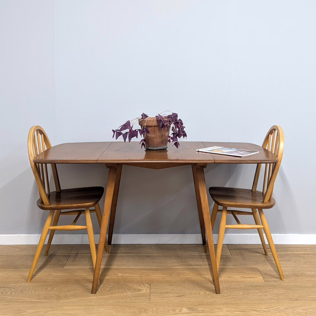 An iconic piece of British mid-century design from Lucian Ercolani in exceptional original condition. Made between 1957 - 1972, this Ercol model 383 plank dining table has two drop leaves so can be set at three different sizes. A really practical design for a more compact dining space or kitchen. It’s made in Ercol’s preferred blonde wood with a solid English elm top and beech splayed legs. These Ercol tables are characterised by their table tops with softly tapered edges that gently slope off. The honey-toned patina of the elm is simply stunning and in our view the grain of vintage Ercol wood is so much more interesting and characterful than its later pieces. A timeless design that never goes out of fashion, an Ercol piece of furniture is for life.